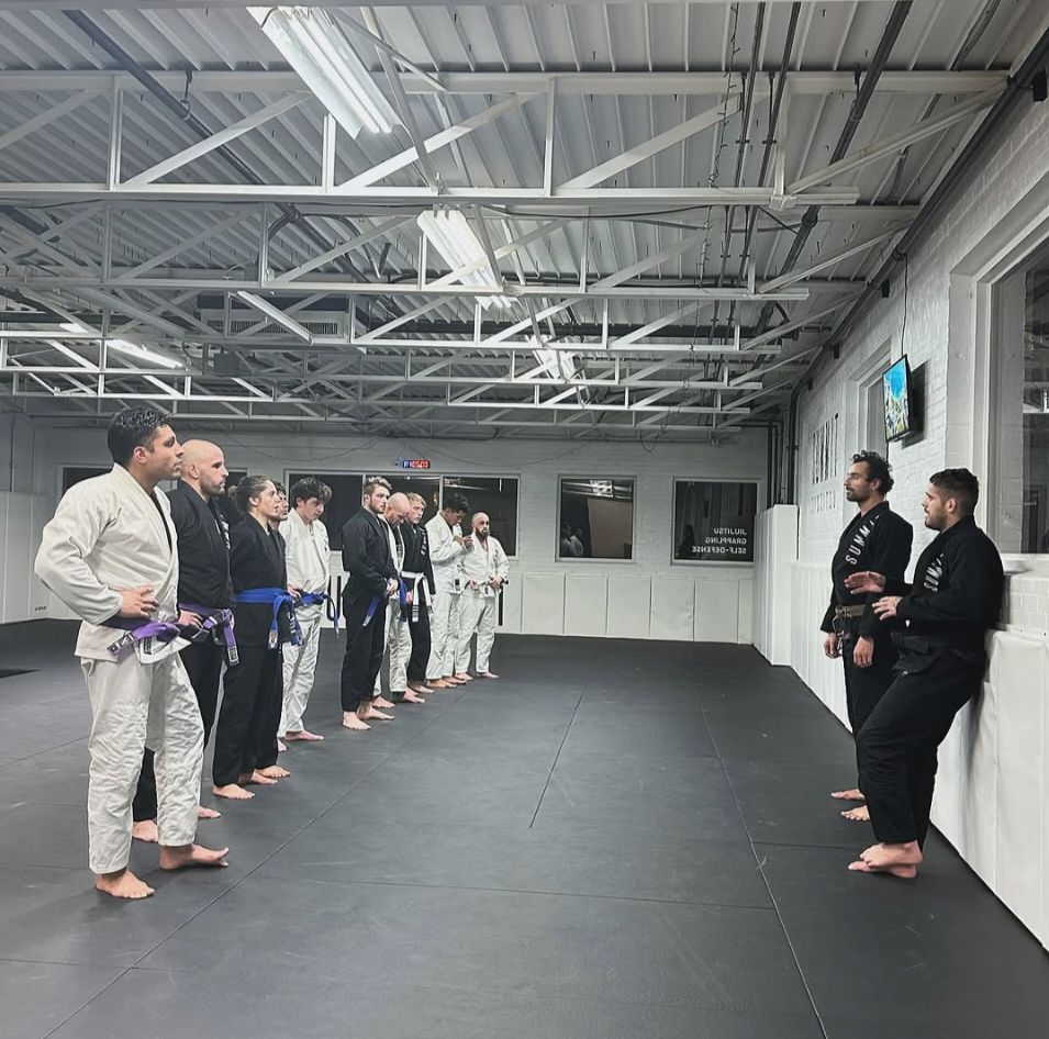 A jiu-jitsu class lined up on the mats, listening to two instructors